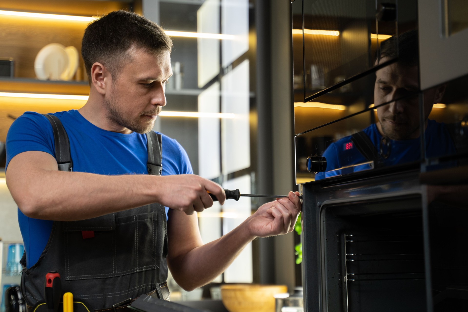 Experienced foreman fixes oven using screwdriver in kitchen