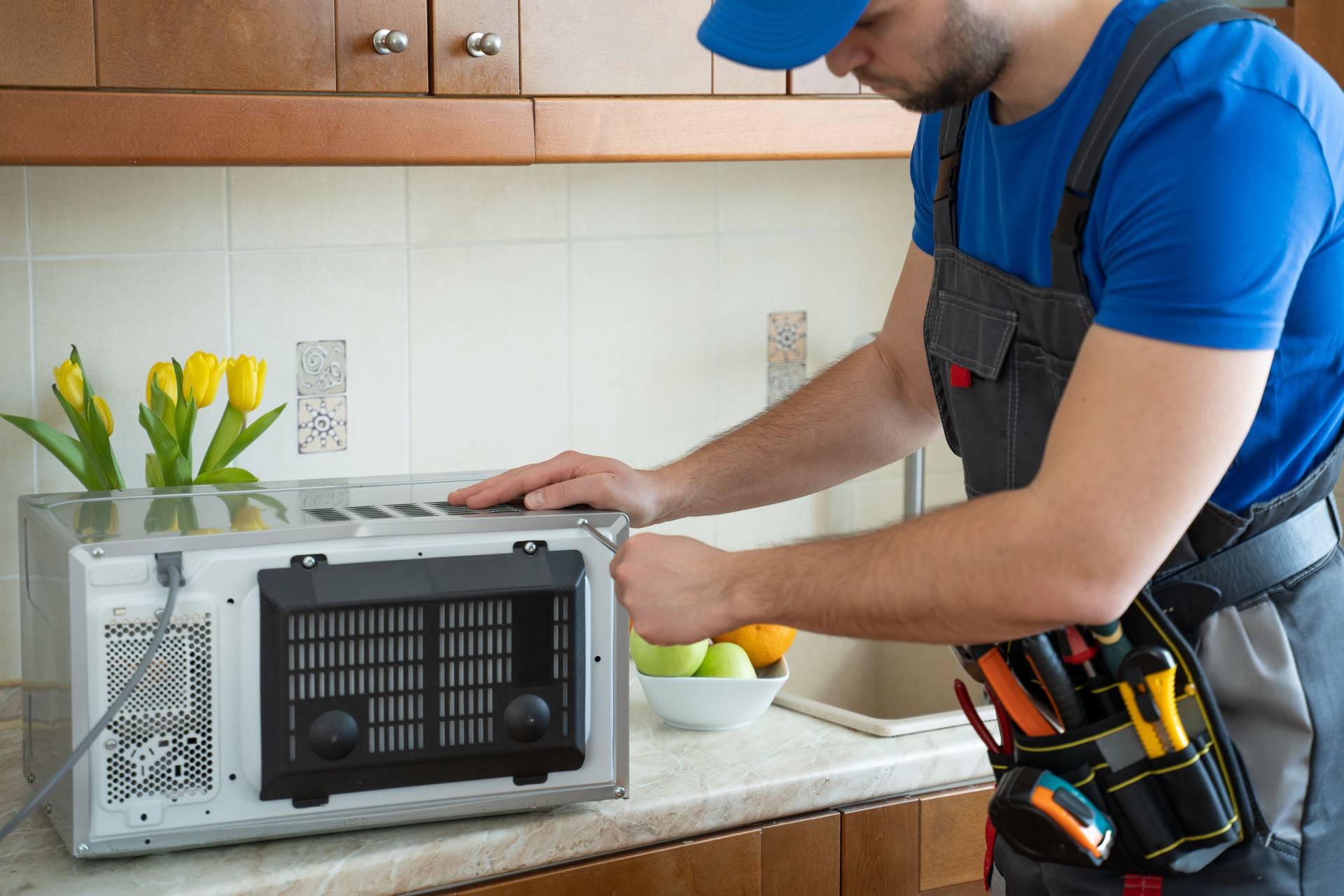 Young repairman fixing and repairing microwave oven by screwdriver in kitchen